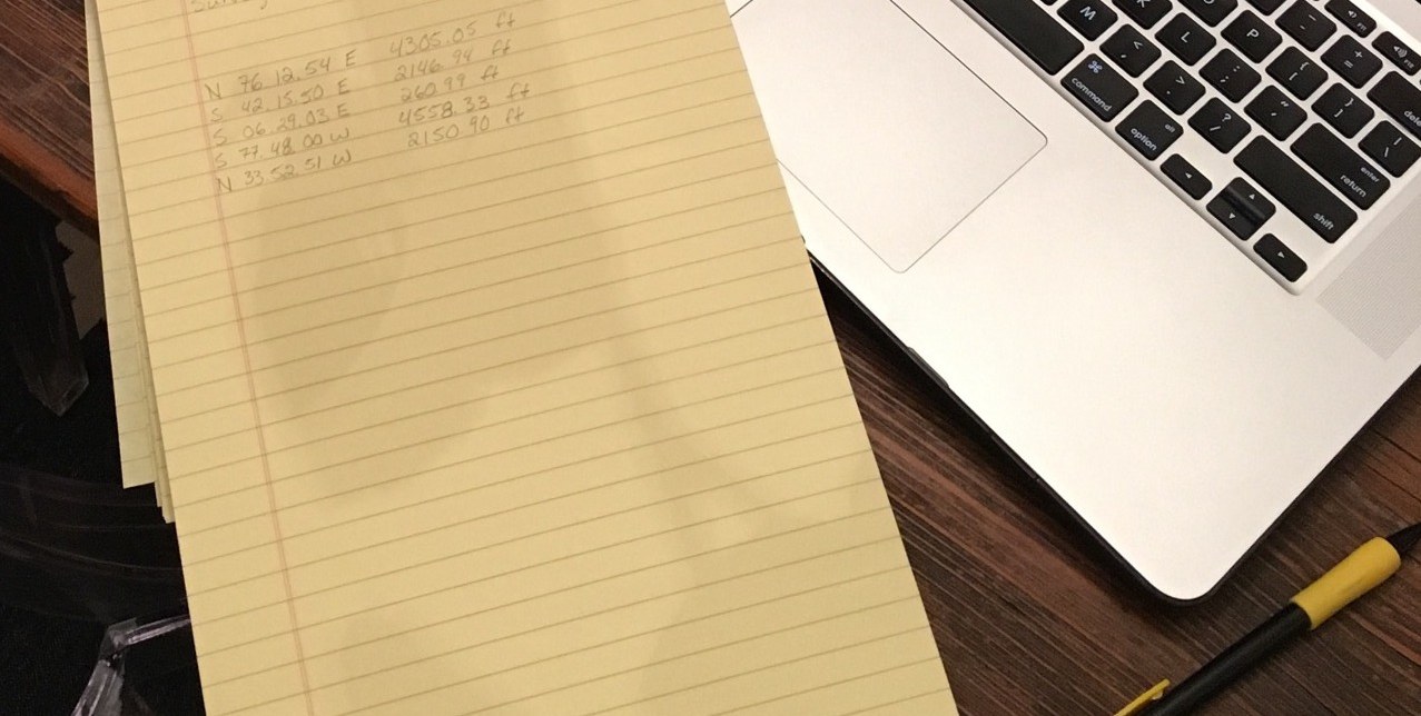 Handwritten survey bearings and distances on a yellow legal pad beside an open laptop